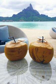 View of two fresh drinking coconuts on a table in front of the Mont Otemanu mountain in Bora Bora, French Polynesia, South Pacific
